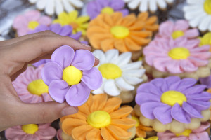 Fancy home made spring flowers sugar cookies with royal icing petals piped on. Young Hand holding purple flower cookie