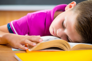 Tired schoolboy sleeping on book in classroom