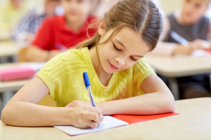 education, elementary school, learning and people concept - group of school kids with pens and notebooks writing test in classroom