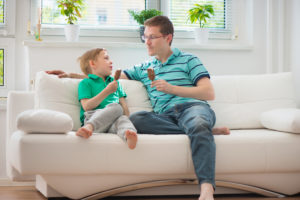 Happy father and little boy eating ice-cream on sofa